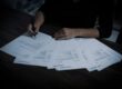 Hands of a person holding a pen over a pile of documents, symbolizing financial preparation and annual report filing in Estonia.